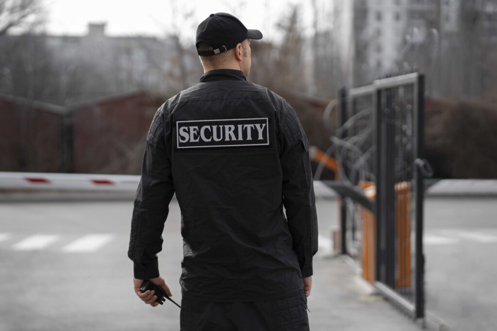 Security guard standing at a gated entrance – cost-benefit comparison of remote video monitoring vs on-site guards by Monitex Security